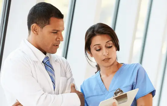 A doctor and a nurse reviewing medical documents together in a hospital setting.