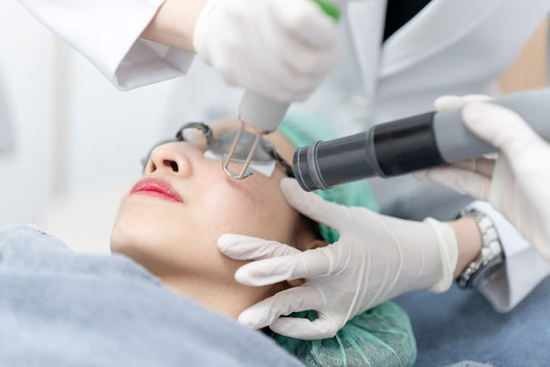 A dermatologist performing a skin treatment on a woman's face using a specialized device in a clinical setting.